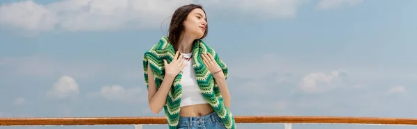 Pretty young woman touching knitted sweater with sky at background, banner — Stock Photo
