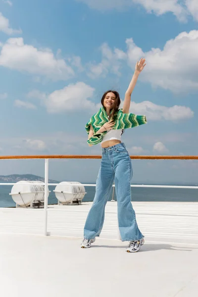 Cheerful young woman in sweater and jeans waving hand while standing on ferry boat in Turkey — Stock Photo