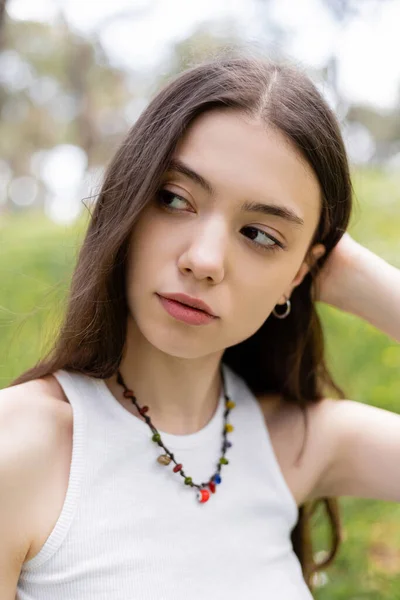 Portrait of young brunette woman in top looking away in blurred park — Stock Photo