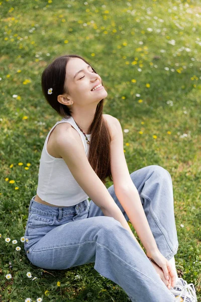 Безтурботний молода жінка в джинсах і зверху сидить на газоні в парку — стокове фото