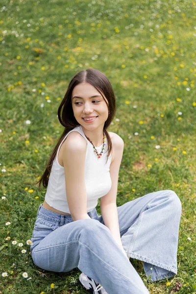 Carefree young woman in casual clothes sitting on meadow with flowers in park — Stock Photo