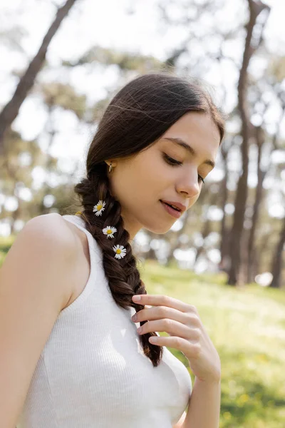 Junge brünette Frau berührt Haare mit Gänseblümchen im Park — Stockfoto