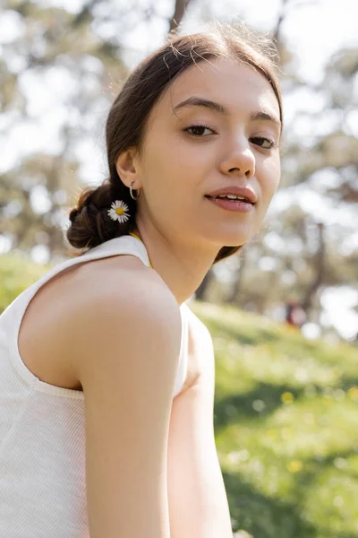Ritratto di giovane donna con fiore in capelli che guarda la macchina fotografica nel parco — Foto stock