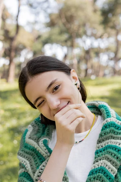 Young woman winking and holding daisy flower in summer park — Stock Photo