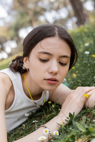 Jovem mulher no topo olhando para flores enquanto deitado no prado no parque — Fotografia de Stock
