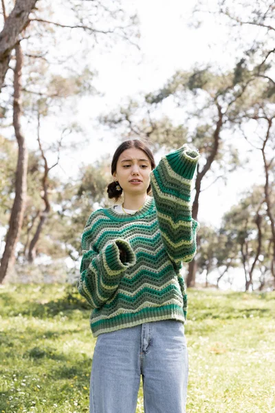 Mujer joven molesta mirando la manga del suéter en el parque de verano - foto de stock