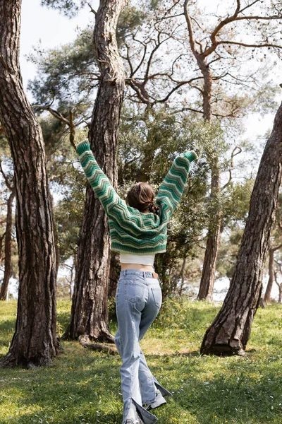 Vue arrière de la femme brune en pull et jeans marchant dans un parc d'été — Photo de stock