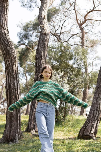 Young brunette woman in knitted sweater walking on lawn in summer park — Stock Photo