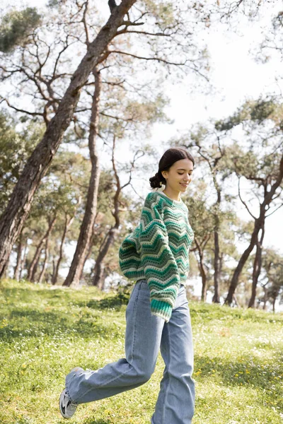 Jeune femme insouciante en pull et jeans marchant sur le parc d'été — Photo de stock