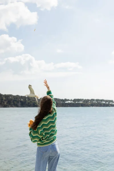 Back view of young woman holding bread near seagull flying over sea in Istanbul — Stock Photo