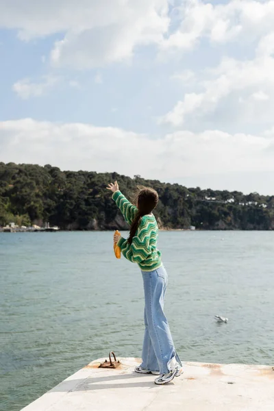 Jeune femme dans une tenue élégante tenant du pain tout en se tenant sur la jetée à Istanbul — Photo de stock