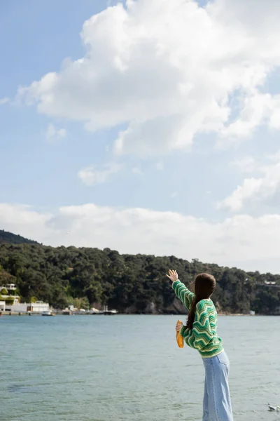 Brunette femme tenant du pain près de la mer avec manteau île princesse en arrière-plan en Turquie — Photo de stock