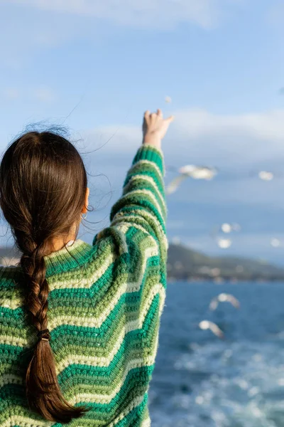 Back view of young woman in sweater outstretching hand and feeding blurred birds in Turkey — Stock Photo