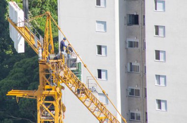 İnşaat alanında vinç taksisinin tepesinde çalışan bir işçi. Üst görünüm.
