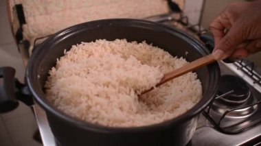 Tavada beyaz pirinç pişiyor. Beyaz pirinç tavada kaşıkla karıştırılıyor.