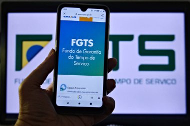 FGTS (Brezilya sosyal güvenlik sigortası) logosu, bir el tarafından tutulan cep telefonunun ekranında. Arka planda Brezilya FGTS logosu var. Rio de Janeiro / Brezilya - 06.30.2024