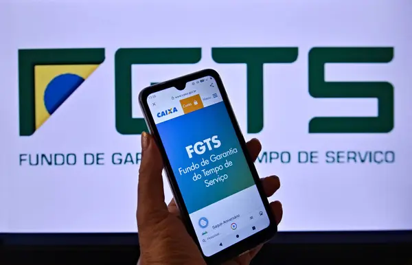 FGTS (Brezilya sosyal güvenlik sigortası) logosu, bir el tarafından tutulan cep telefonunun ekranında. Arka planda Brezilya FGTS logosu var. Rio de Janeiro / Brezilya - 06.30.2024