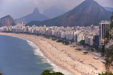 Copacabana sahilinde kum, deniz ve kıyı ön planda ve dağlar ve arka planda mavi gökyüzü. Hava görünümü.