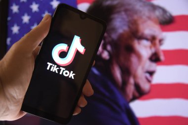 Ekranda TIKTOK uygulaması logosu olan akıllı telefon ve arka planda seçilmiş başkan Donald Trump ve ABD bayrağı. Teknoloji, sosyal medya ve ticaret anlaşmazlığı kavramı. Rio de Janeiro, Brezilya - 01.16.2025.