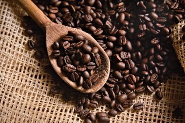  Kır bezi yüzeyinde kavrulmuş kahve çekirdekleri ve ahşap bir kaşık. Kahve çekirdeği ve yemek pişirme kavramı