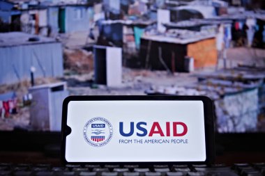 Cell phone with the United States Agency for International Development (USAID) seal in the foreground and a scene of poverty (slum) in the background. Rio de Janeiro, Brazil - 02.04.2025 clipart