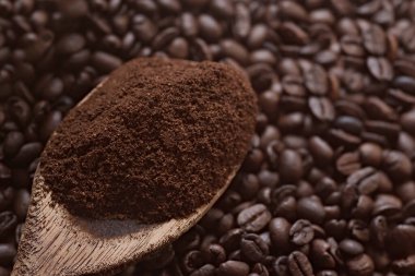 Kavrulmuş kahve çekirdekleri ve ahşap bir masada öğütülmüş kahve. Tahta kaşık ve içinde kahve var..