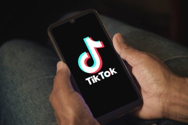 Ekranda TikTok logosu olan cep telefonu tutan bir kadın. Bir kadın evde dinlenirken akıllı telefonunda TikTok uygulamasını kullanıyor. Sosyal medya konsepti. Rio de Janeiro, Brezilya - 03.29.2025