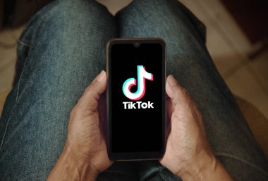 Ekranda TikTok logosu olan cep telefonu tutan bir kadın. Bir kadın evde dinlenirken akıllı telefonunda TikTok uygulamasını kullanıyor. Sosyal medya konsepti. Rio de Janeiro, Brezilya - 03.29.2025