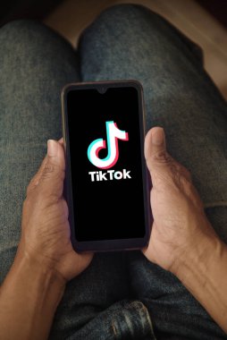 Ekranda TikTok logosu olan cep telefonu tutan bir kadın. Bir kadın evde dinlenirken akıllı telefonunda TikTok uygulamasını kullanıyor. Sosyal medya konsepti. Rio de Janeiro, Brezilya - 03.29.2025