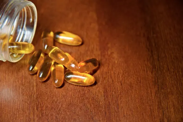 Balık yağlı sarı jelatin kapsüller, veya D3 vitamini, ve masanın üzerinde açık şişe. Aşırı doz, zehirlenme, ilaçlardan kaynaklanan zarar..