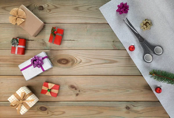 Handmade items and decorated gift boxes. Flatlay. DIY gift wrapping concept at home. Wrapping paper, fir branch, Christmas balls, scissors, colorful boxes with gifts on wooden background. Copyspace. Top view.