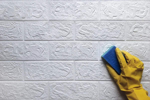 Cleaning process - hand in yellow rubber glove with sponge washes white brick wall. Space for text. Theme of spring cleaning, perfect cleanliness, disinfection and dirt control. Copy space Flat lay.