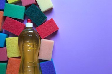 Minimum set for cleaning in office, cafe, restaurant, home. Space for text. Flatlay. Bright kitchen sponges around bottle of detergent on purple background with with copy space. Top view.
