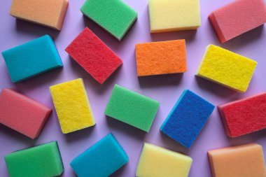Background from kitchen sponges. Top view. Housecleaning concept. Multi colored washcloths for cleaning are scattered on purple surface. Flat lay. Template for banner, advertising, packaging.