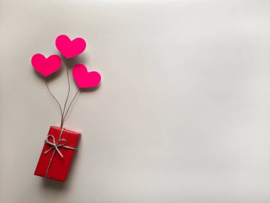Selection, purchase, packaging, delivery of gift for birthday, anniversary, jubilee. Top view. Copy space. Red gift box on pink balloons in form of hearts on light background. Flat lay. Space for text