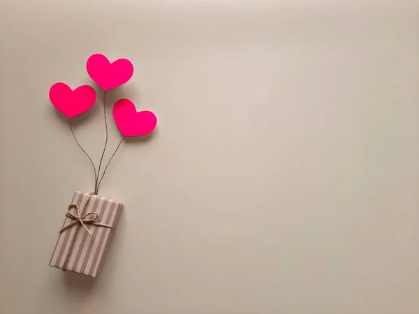 Selection, purchase, packaging, delivery of gift for holiday, mother's day. Top view. Copy space. Gift in a striped box on balloons in form of hearts on light background. Flat lay. Space for text