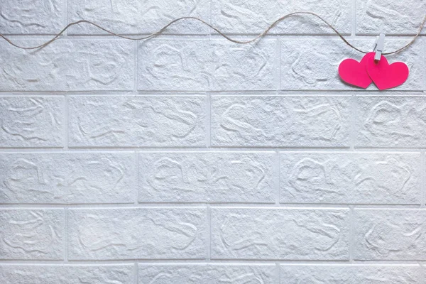 oncept of love, romance, wedding. Valentine's day page. Space for text. Two pink hearts on clothespins hang on rope in right corner on white brick background. Template for romantic activities, events.