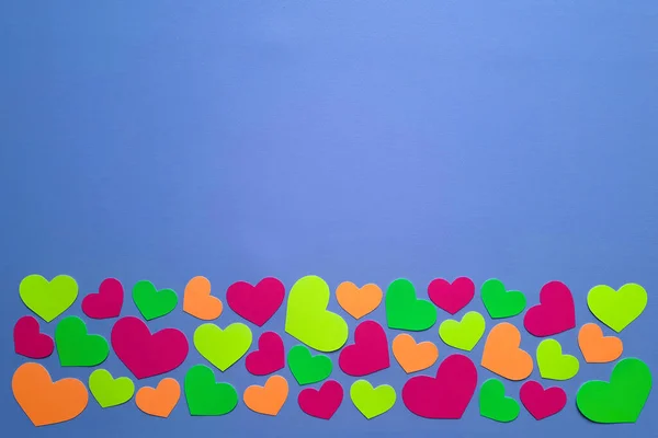 Template for card, advertisement, invitation to party, birthday, holiday. Place for text. Neon confetti in heart form shape over blue background with copy space. Valentine's day page. Flat lay.