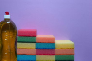 Steps made of multi colored kitchen cleaning sponges and detergent on purple background with place for text. Home cleaning service concept. Cleanup schedule, helping children with household chores.