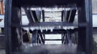 Old wooden wheel of water mill rotates in stream of river. Falling drops. Concept of past and future technologies, technical progress. Mechanisms in human life. Energy of nature and industry.