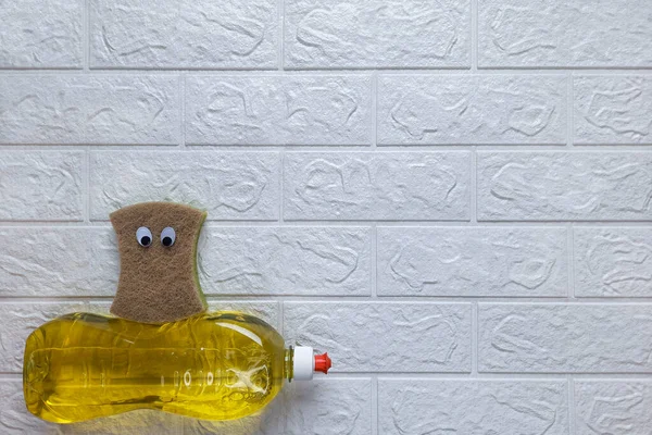 Funny composition and homework clean up. Top view. Copy space. Fun cleaning. Kitchen sponge with eyes sits on detergent on white brick wall background. Flat lay. Template for advertisement, billboard.