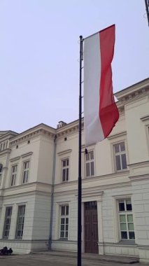Poland flag flying on cloudy weather in slo-mo. Vertical video. Red and white stripe. Official symbol of Poland on flagpole on cloudy day against backdrop of ancient building in European city.