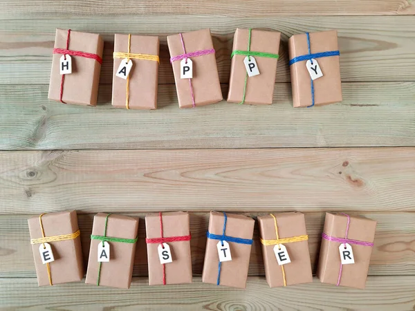 Easter gift boxes. Copyspace. Top view. Template for card, advertising, events, discount. Boxes wrapped in craft paper with labels saying Happy Easter lie on wooden table. Space for text. Flat lay. 