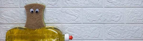 Funny banner with concept fun cleaning. Top view. Copy space. Cartoon kitchen sponge with eyes sits on detergent on white brick wall background. Flat lay. Heading for site, blog, article, polygraphy.