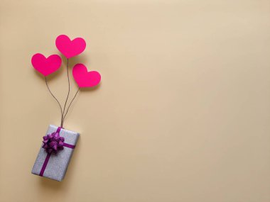 Balonların üzerinde parlak gümüş bir hediye kutusu var. Arka planda kalp şeklinde. Düz yatıyordu. Mesaj seçimi, satın alma, paketleme, Anneler Günü için hediye teslimatı, doğum günü için yer. Üst Manzara. Boşluğu kopyala.