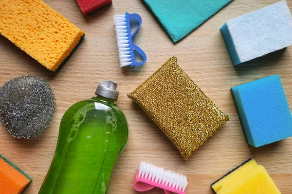 Background with Essential Cleaning Tools. Flat lay desing. Kitchen sponges, scrubbing brushes, metal dishwashing sponge, rags, detergent on a wooden table. Variety of household cleaning products.