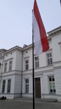 Polonya bayrağı rüzgarda dalgalanırken gökyüzüne karşı bulutlarla, eski bir binanın arkaplanıyla. Bir Avrupa ülkesinin ulusal sembolü kırmızı ve beyaz bir sancaktır. Dikey video.