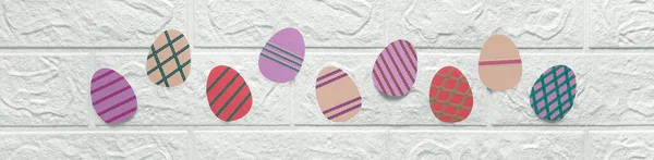 Renkli kartondan yapılmış Paskalya yumurtaları olan pankart. Anaokulu, okul, sanat sınıfı için tematik başlık. Beyaz duvarın arkasındaki kağıttan kesilmiş desenli çok renkli yumurtalar. Çocuklar için el sanatları