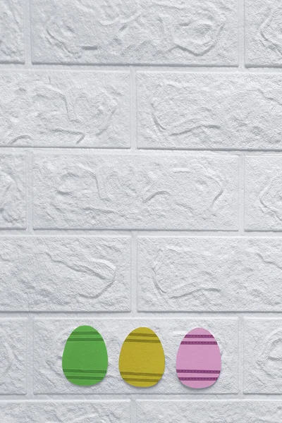 Basit Paskalya Süslemeleri. Uzayı kopyala Üst Manzara. Mutlu Paskalyalar. Beyaz duvarın arka planında el yapımı kartondan kesilmiş üç Paskalya yumurtası. Düz yatıyordu. Mesaj için yer. Dikey şablon.