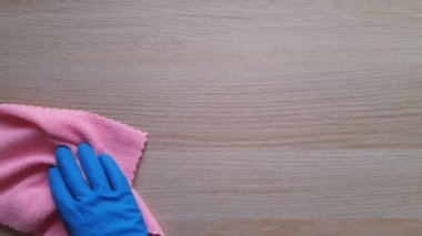 Evi temiz ve düzenli tutmak için günlük alışkanlıklar. Zaman kazandıran temizlik ipuçları. Mavi plastik eldiven ve pembe sentetik mikrofiber kumaş, ahşap masayı siler. Toprak ve tozun kaldırılması. Reklam için parça.